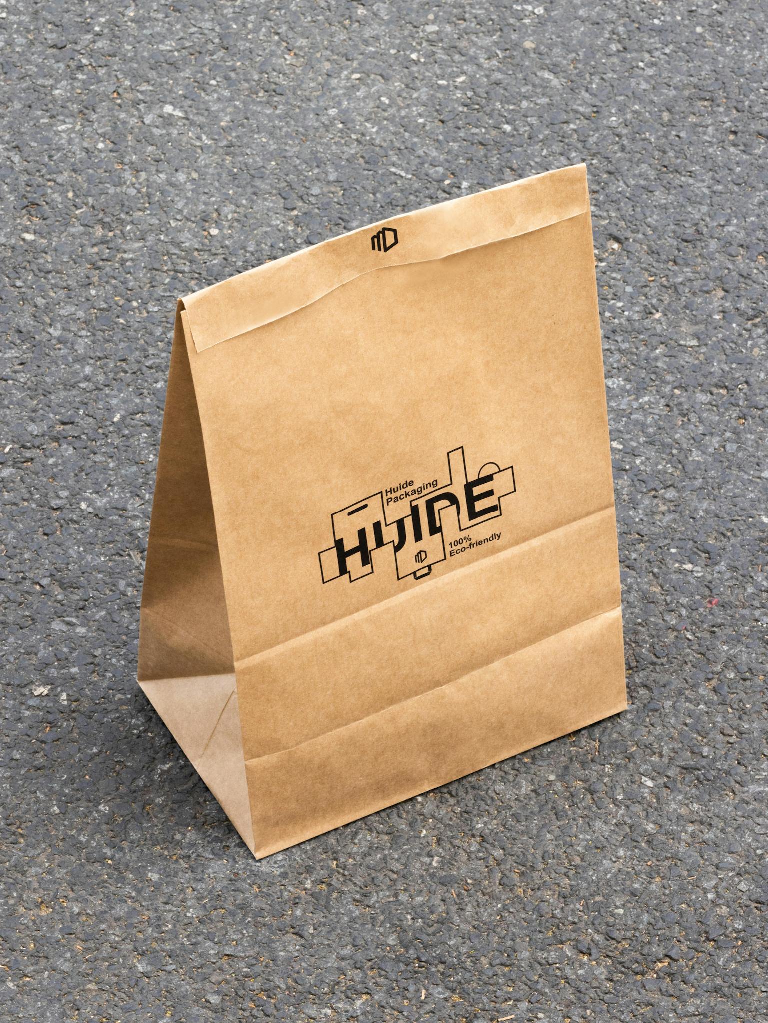 A standing kraft paper bag with custom print on a textured asphalt surface under sunlight.